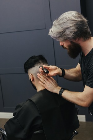 Male barber combing and shaving hair of a male client at barbershopの写真素材