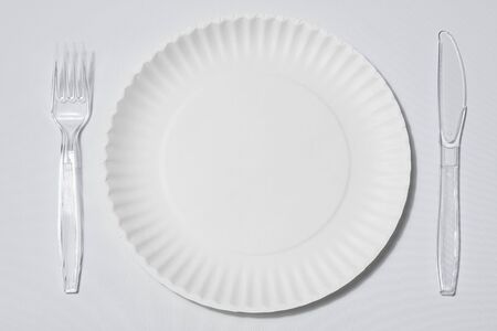 empty singleuse white paper plate with set of clear plastic fork and knife on white background or tableclothの写真素材