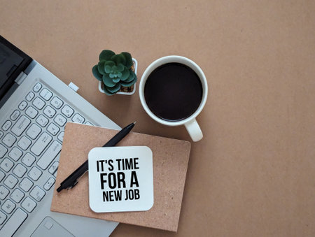 Flat lay view of laptop, a cup of coffee, computer, pen , plant in pot and notebook with text IT'S TIME FOR A NEW JOB.の写真素材