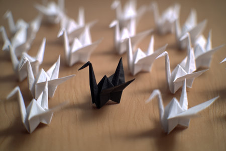 A striking black origami crane stands out amidst dozens of white origami cranes, beautifully arranged on a wooden tabletop, showcasing creativity and craftsmanship.の素材