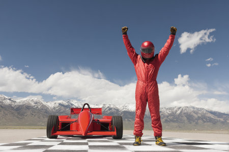 A confident racer celebrates triumph in victory pose on the podium with arms raised, capturing the excitement of success at the end of the track.の素材