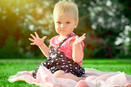 cute playful blond 1 2 years old girl sitting on green grass outdorの写真素材