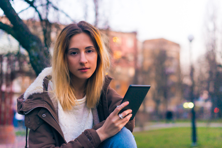 Young woman using tablet outdoor sitting on bench, smiling.の写真素材