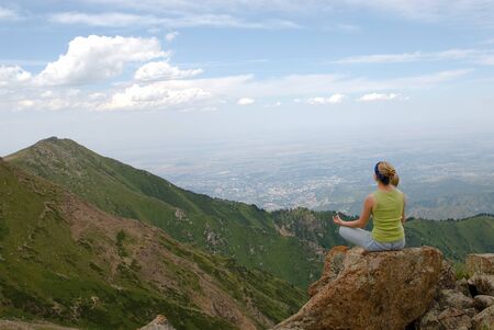 The young girl sits in a position of a lotus on high mountainの写真素材