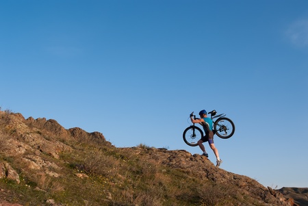 Bicyclist carries its mountain bicycle on whirlled rocky declivityの写真素材