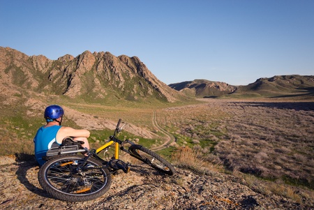 Bicyclist admires mountain terrain illuminated evening sunの写真素材