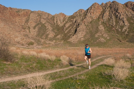 The athlete runs on the mountain road shined with the evening sun
