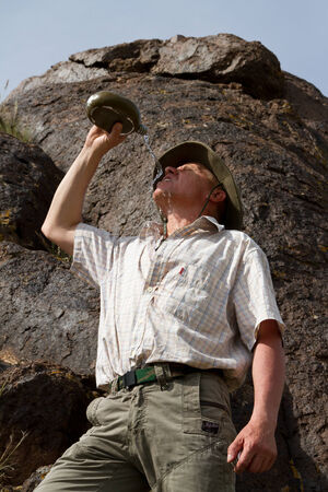 the traveler drinks water from a flask on a strong blaze of the sunの写真素材