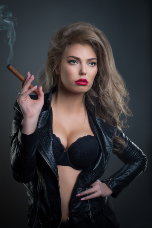 Sexy young woman with sigar on dark background studio shot photoの写真素材
