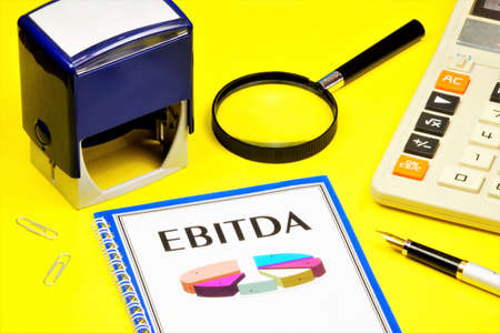 EBITDA-a text inscription on the letterhead of the folder and a graph indicator of the company's valuation. Calculator for calculations, printing and pen for visa documents.の写真素材