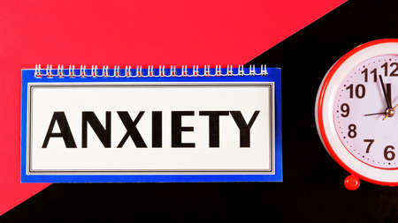 Anxiety - text message in Notepad on a creative background. Negative emotion, feeling of uncertainty, expectation of adverse events. The clock is a symbol of time, reminding of the past and future.の写真素材