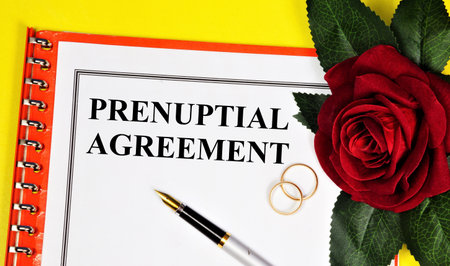 Prenuptial agreement. Text inscription on the form of the document. Wedding rings and red rose holiday decoration.の写真素材