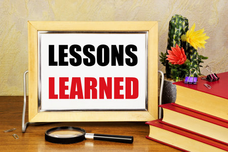 Lessons learned. The inscription in the plate on the background of textbooks. Knowledge gained from experience, for improving activities in the future.の写真素材