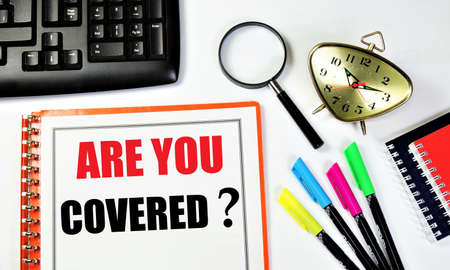 Are you covered? An inscription in the planning folder, against the background of a time control clock, magnifying glasses for research, a computer keyboard, colored markers and a notepad.の写真素材