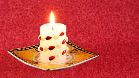 A bright candle in a vintage candlestick, illuminates the free space of a red bokeh background for creative design and writing metaphor text.の写真素材