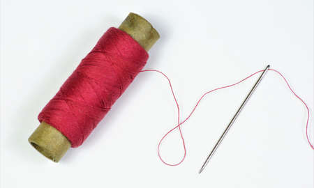 The sewing needle is a pointed tool and a red thread threaded into the eye of the needle. Designed for stitching clothing parts.の写真素材