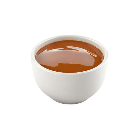 Small, round, white bowl is filled with a smooth, caramel-colored liquid,  placed against a plain white background.  The liquid appears to be a sauce or a dessert topping.の素材