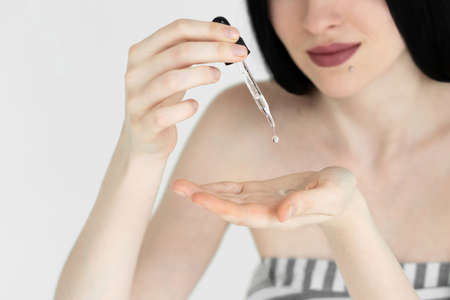 A pipette with a drop of serum in the girls hand. Close-up. Beauty therapy concept. Grey background.