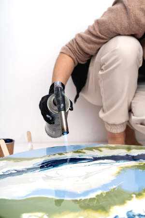 The process of creating a painting using fluid art technique. Female hands with gas burner.の写真素材