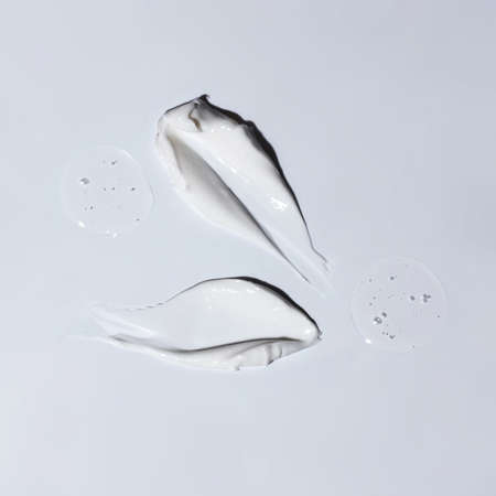 Sample of white cosmetic cream, drops of gel and foam on a gray background.