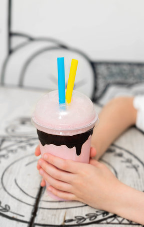 In the hands of the child a glass with a cocktail and straws standing on a tableの写真素材