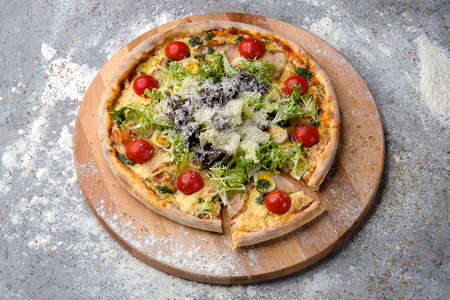 Whole Pizza on wooden plate served with culinary flour and spices on gray concrete background. Fast food dish with fresh lettuce, cherry tomatoes, quail eggs, Parmesan cheese, chicken filletの写真素材