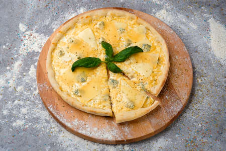 Whole classic Four cheese Pizza with Parmesan, Gouda, mozzarella and blue cheese served with fresh basil leaf on top on wooden plate served with culinary flour and spices on gray concrete background.の写真素材