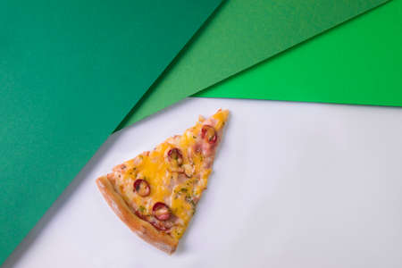 Close up of Cheesy slice of meat pizza with hunting sausages, cheese and basil pesto sauce on light...