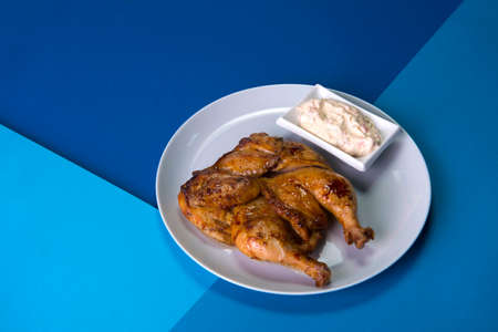 Grilled chicken Tabaka on gray plate served with sauce in white bowl. Georgian cuisine. Restaurant menu food on blue abstract backgroundの写真素材