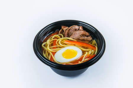 Beef Udon Soup with egg, udon noodles and beef fillet, paprika (bell pepper) served in plastic delivery bowl. Dish isolated on gray background. Asian first dish in black plate. Food isolationの写真素材