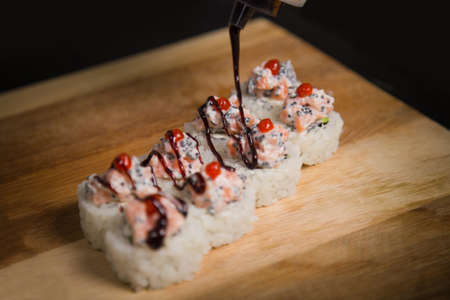 Cooking process of serving Japanese volcano sushi roll with unagi sauce. Pan Asian dish on wooden board. Sake salmon roll piece with rice and flying fish roe (tobiko). Restaurant food compositionの写真素材