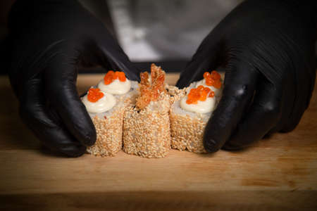Chefâ€™s hands in black protective gloves near traditional Ebi Tempura Sushi Roll with tempura...