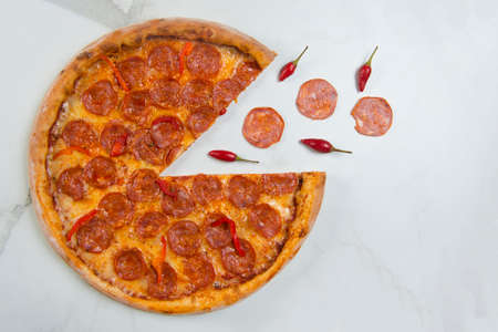 Classic Italian spicy Pepperoni Pizza with salami slices and mozzarella cheese on white marble background with ingredients. Flying food concept. Fast food dish served with Chilli pepperの写真素材