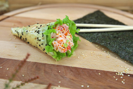 Japanese Temaki Sushi Hand Roll with crab meat sticks, avocado, flying fish roe Tobiko wrapped in lettuce leaves, rice and Mamenori served on wooden board. Nori seaweed sheet, chopsticks on backgroundの写真素材