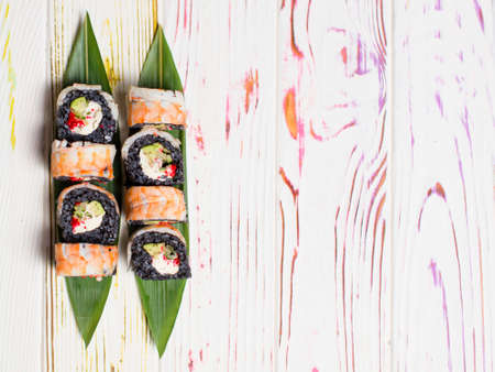 Directly above of Japanese black rice sushi roll with shrimp on top served on bamboo leaves on colorful light wooden background. Avocado wrapped in black riceの写真素材