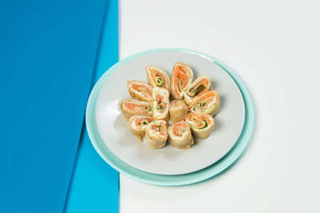 Side view of crepe pieces. Salmon, cucumber, cream cheese wrapped in crepes. Seafood Russian holiday isolated dish served on blue background. French Appetizer. Food creative serving of cold starterの写真素材