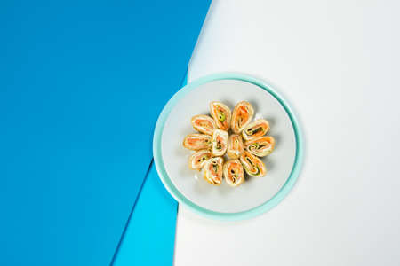 Top view of crepe pieces. Salmon, cucumber, cream cheese wrapped in crepes. Seafood Russian holiday isolated dish served on blue background. French Appetizer. Food creative serving of cold starterの写真素材