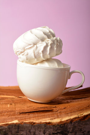 Old cup filled with souffle airy dessert zefir (zephyr) made of organic pectin and egg whites, similarly to marshmallow and meringue. Served on wooden log on violet (lavender) pastel backgroundの写真素材