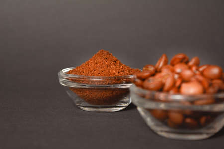 Ground (grinded) coffee served in glass bowl with Roasted coffee beans in bowl out of focus on dark background. High quality organic aroma seeds. Copy space text imageの写真素材