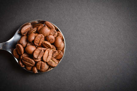 Top view of Roasted coffee beans served in silver vintage stainless steel spoon on dark background. High quality organic aroma seeds. Copy space text imageの写真素材