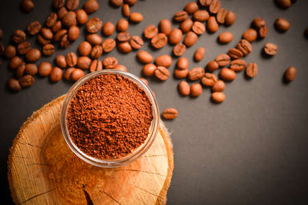Ground coffee served in glass bowl on wooden log with scattered coffee. High quality organic arabica seeds. Roasted coffee beans on dark background out of focus. Copy space text imageの写真素材