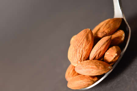 Close-up Almond nuts served on silver metal stainless steel spoon. almonds on dark background. Creative food concept. Raw nuts. Copy space image. Single object. Kitchen still lifeの写真素材
