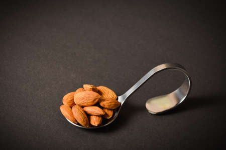 Horizontal image. Side view of Almond nuts served on silver metal stainless steel spoon. almonds on dark background. Creative food concept. Raw nuts. Copy space image. Single object. Kitchen still lifeの写真素材