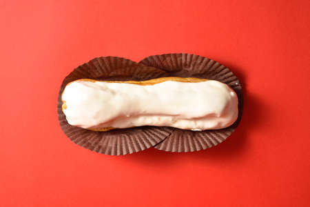 Classic French dessert eclair with white chocolate on top filled with custard, served on red background. Top view. Copy space imageの写真素材
