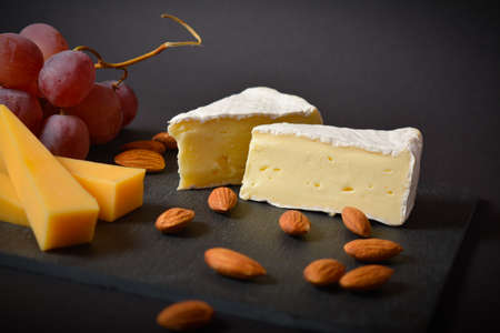 Tasty healthy cheeseboard with hard and soft cheese, pink grapes and almonds. White mould french...