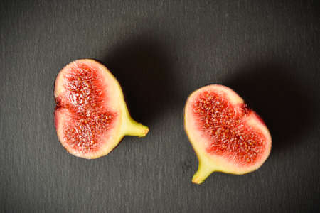 Top view of two halves of Azerbaijani fig fruit. Exotic eastern fruit. Segmented berry isolated on black stone backgroundの写真素材