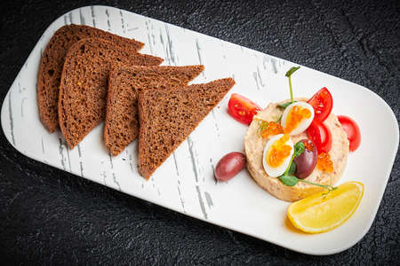 Jewish traditional dish Forshmak on white plate on black background. Herring Fish Vorschmack served with dark whole rye bread slices. Fish pate served with cherry tomatoes, quail eggs, salmon caviarの写真素材