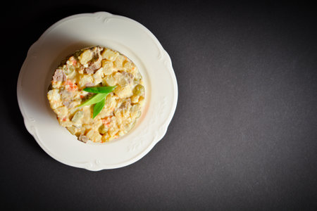 Top view of traditional Russian Olivier salad. Soviet dish served in glass bowl on black background. Salad with green peas, potato, carrot, egg and meat cubes with mayonnaise sauce dressingの写真素材