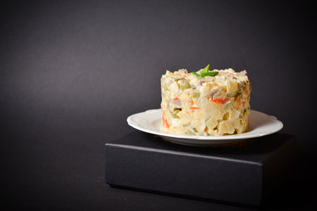 Side view of salad Olivier served in culinary ring with green onion on top. Dish located on a black box. Copy space image with space for text with dark background. Russian Salad with boiled vegetablesの写真素材
