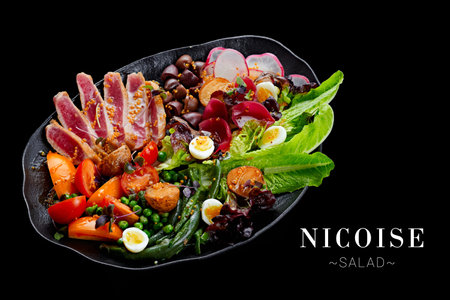 Side view of traditional French Nicoise salad with roasted tuna potato, tomato, lettuce, olives and quail eggs served on platter isolated on black background. Ready menu banner with text, copy spaceの写真素材